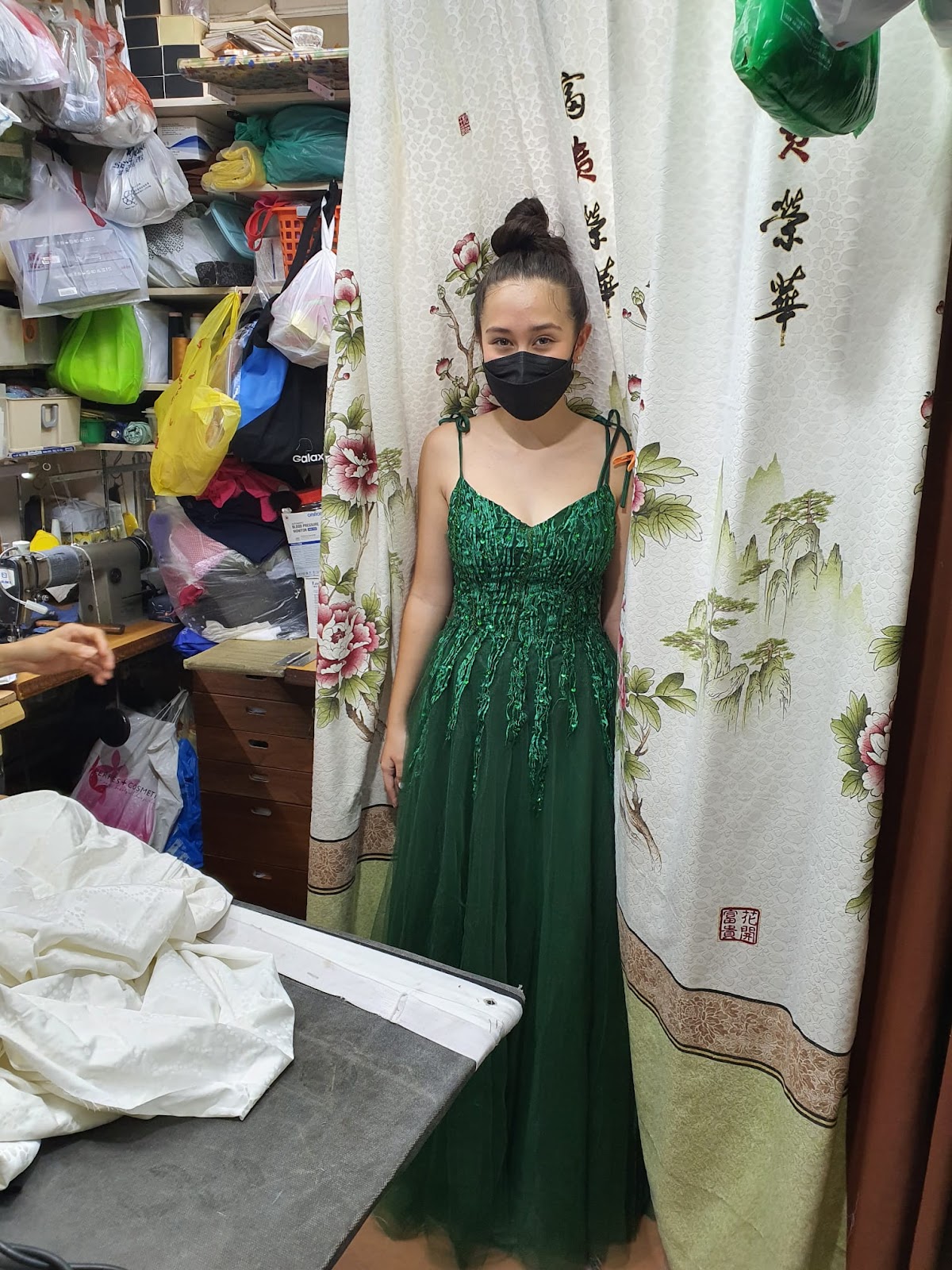 A customer in an altered emerald evening gown at the shop's fitting curtain