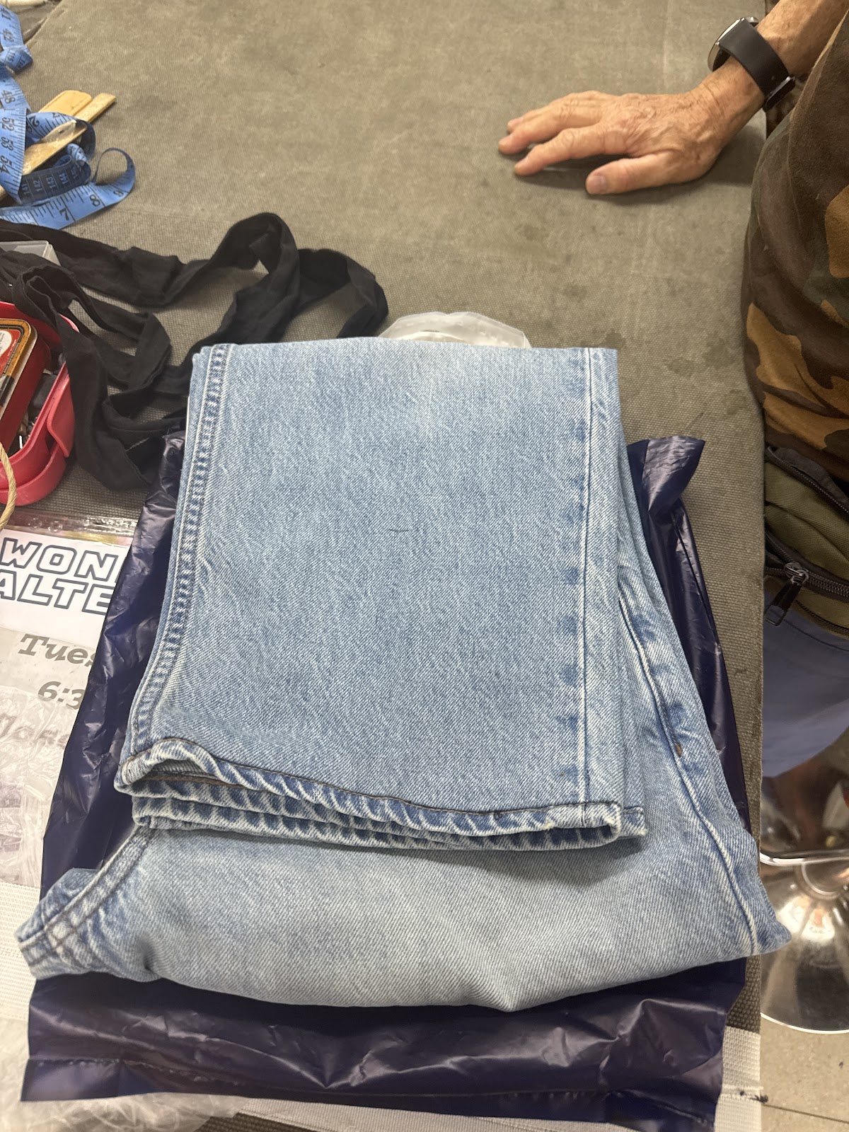 Freshly altered jeans folded on the counter, measuring tape alongside