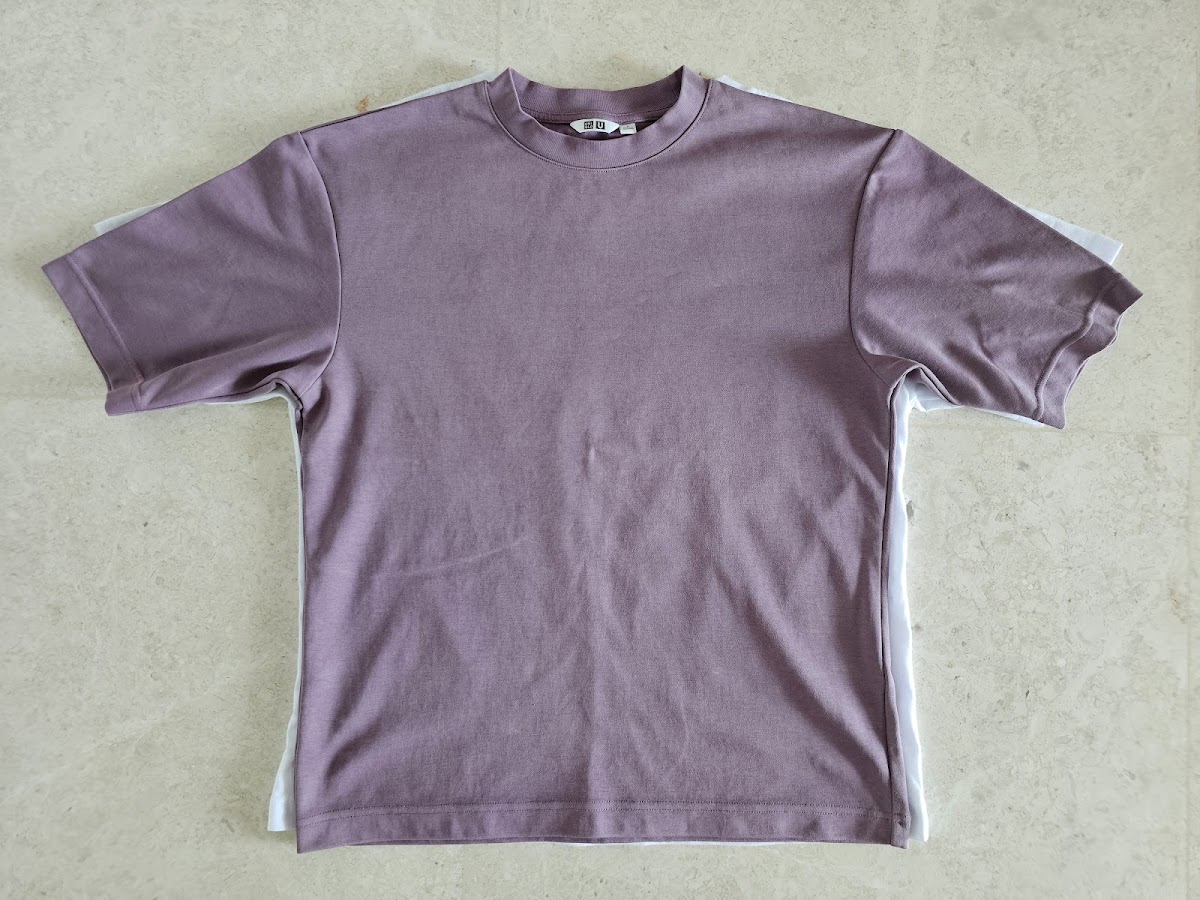 A resized purple t-shirt laid flat on top of the original, larger one